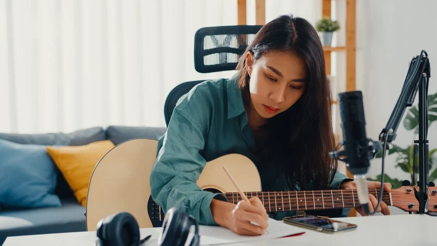 Jovem mulher fazendo anotações e aprendendo a tocar violão
