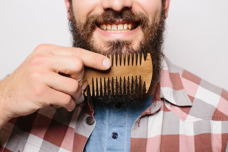 Homem sorrindo ao utilizar um pente de madeira para pentear sua barba