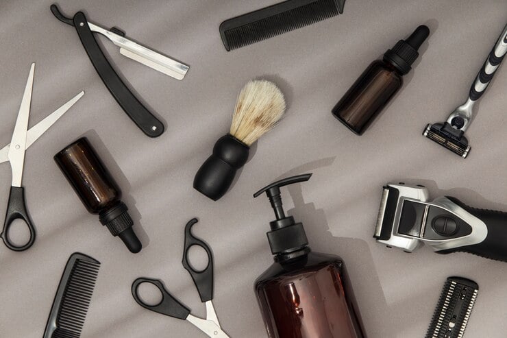Produtos de cuidados com a barba espalhados numa mesa. Alguns produtos visíveis são: barbeador elétrico, tesoura, lâmina de barbear, pente e embalagens de shampoo e óleo para barba.