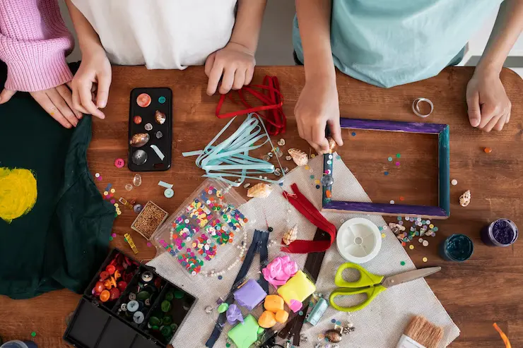 Crianças mexendo em uma mesa com artefatos e materiais de colagem para projetos DIY