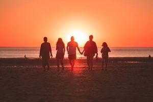 familia caminha na praia com por do sol de fundo